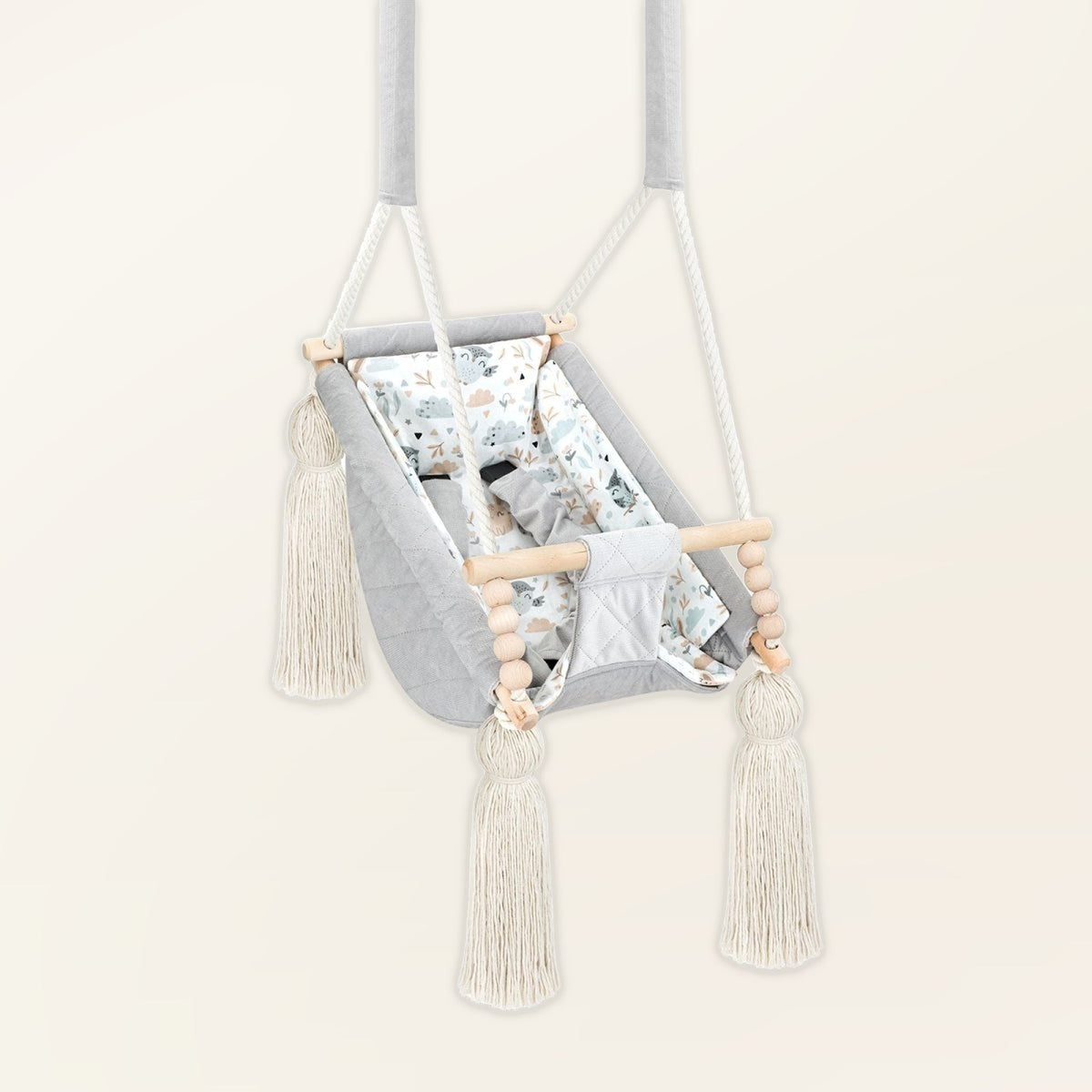 Hamac bébé suspendu en velours gris clair, vue de trois quarts : pompons, perles en bois et assise rembourrée