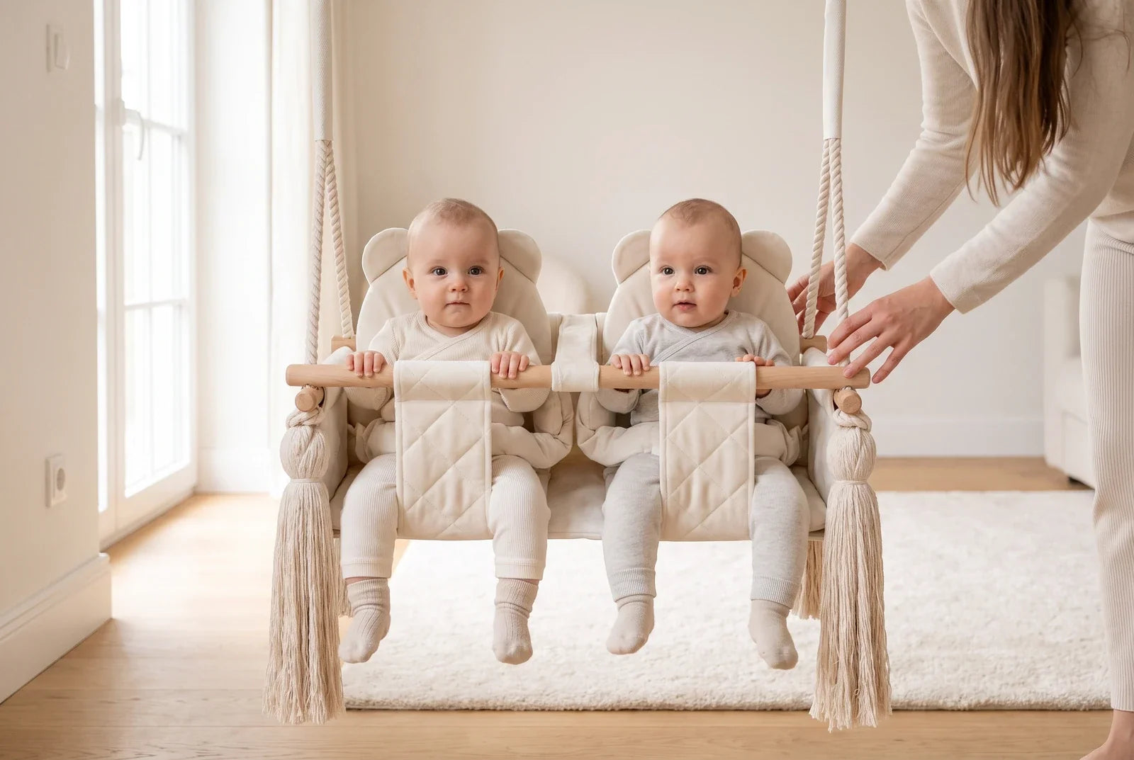 Deux bébés assis chacun dans un siège de la balançoire double en velours beige, un adulte à côté d'eux