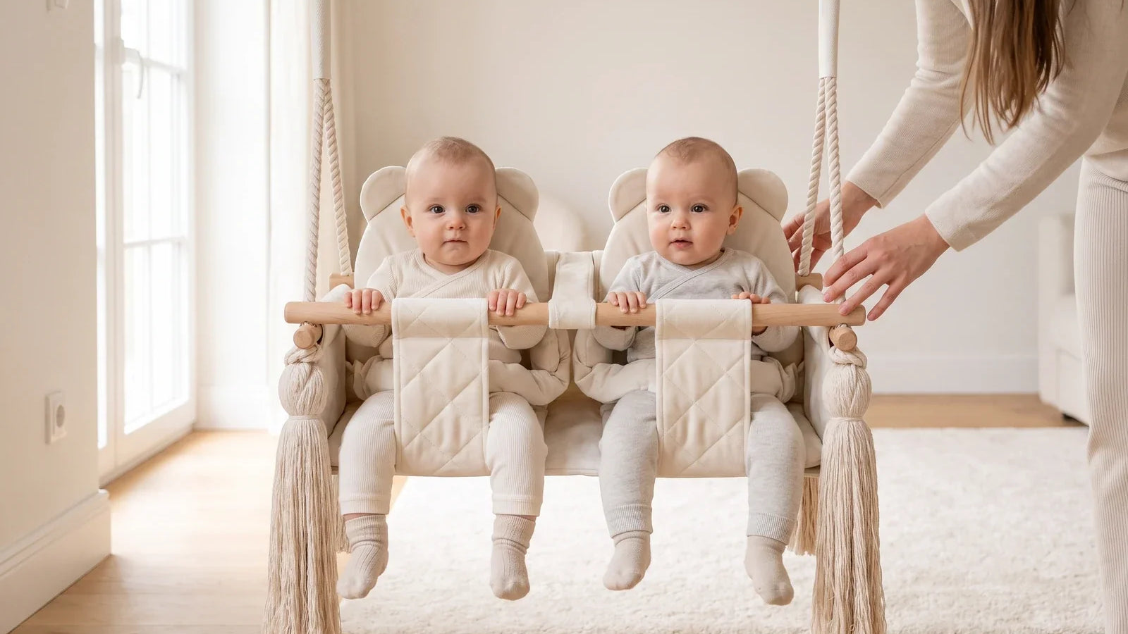 Deux bébés assis chacun dans un siège de la balançoire double en velours beige, un adulte à côté d'eux