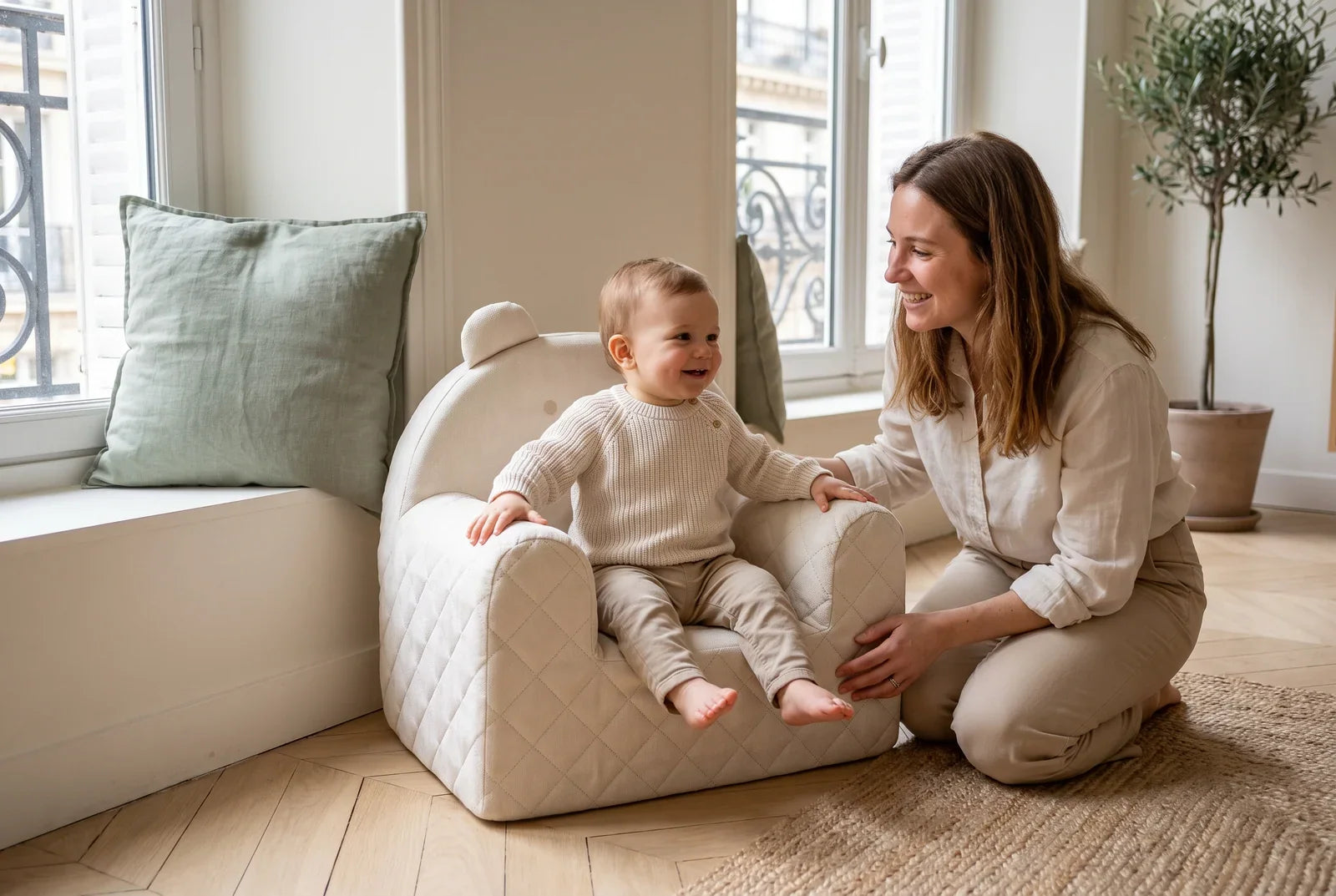 Enfant d’environ un an assis dans un fauteuil ourson beige en velours, sa maman agenouillée à côté de lui