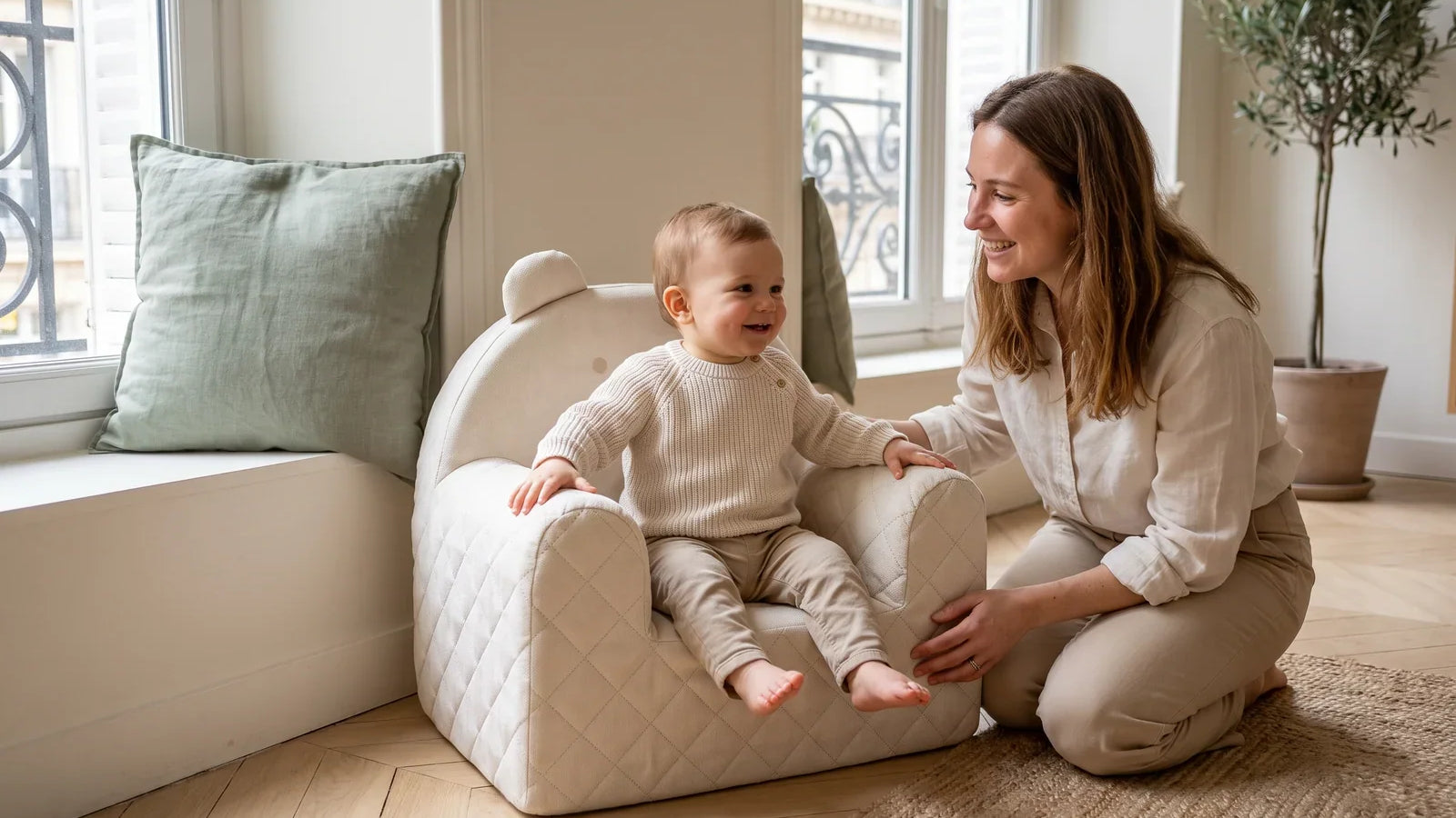 Enfant d’environ un an assis dans un fauteuil ourson beige en velours, sa maman agenouillée à côté de lui