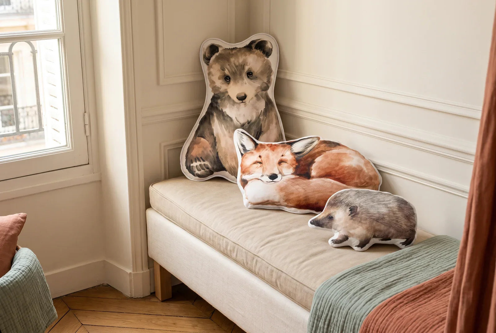 Coussins ourson, renard et hérisson en velours posés sur une banquette beige dans une chambre d'enfant