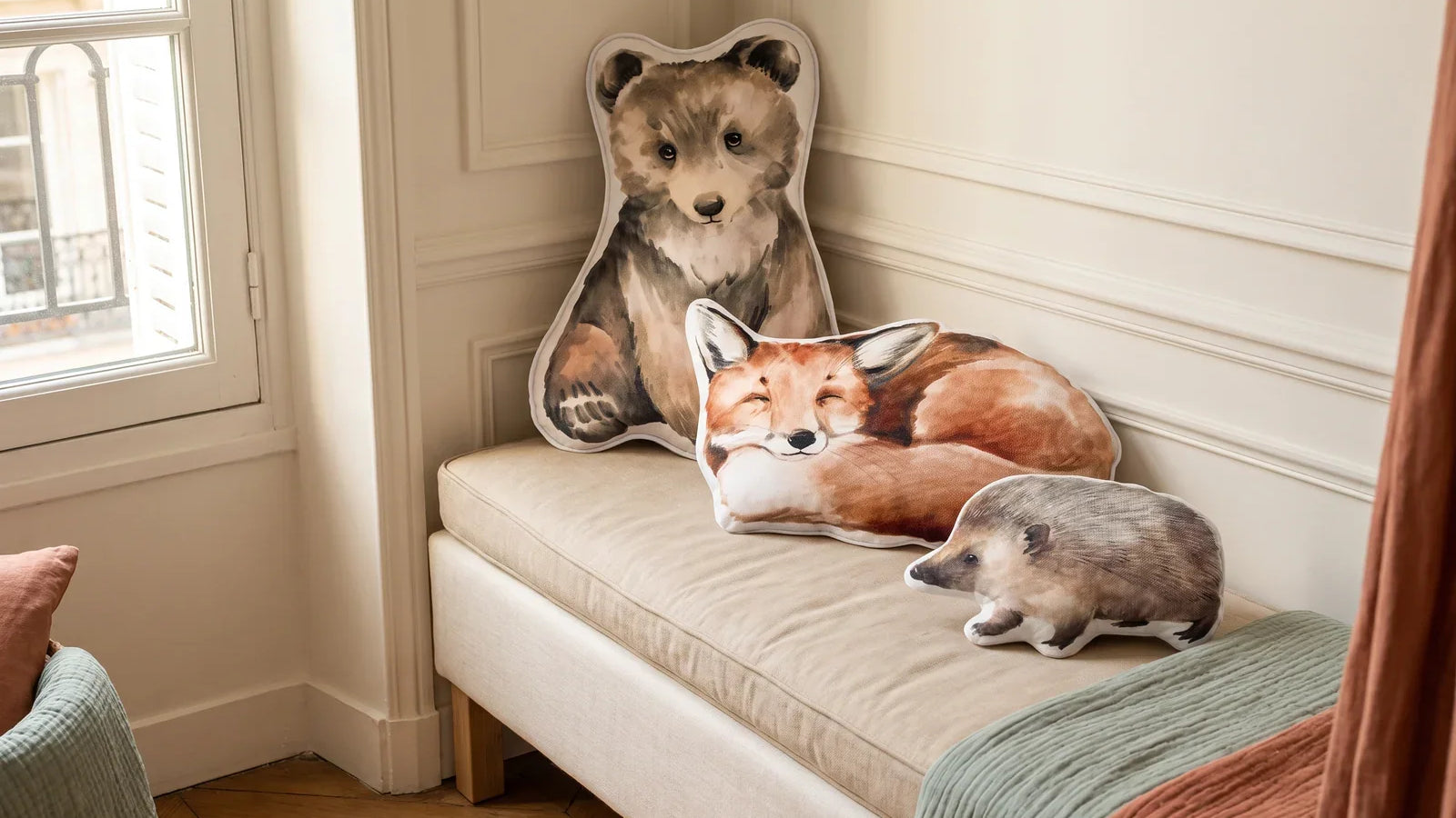 Coussins ourson, renard et hérisson en velours posés sur une banquette beige dans une chambre d'enfant