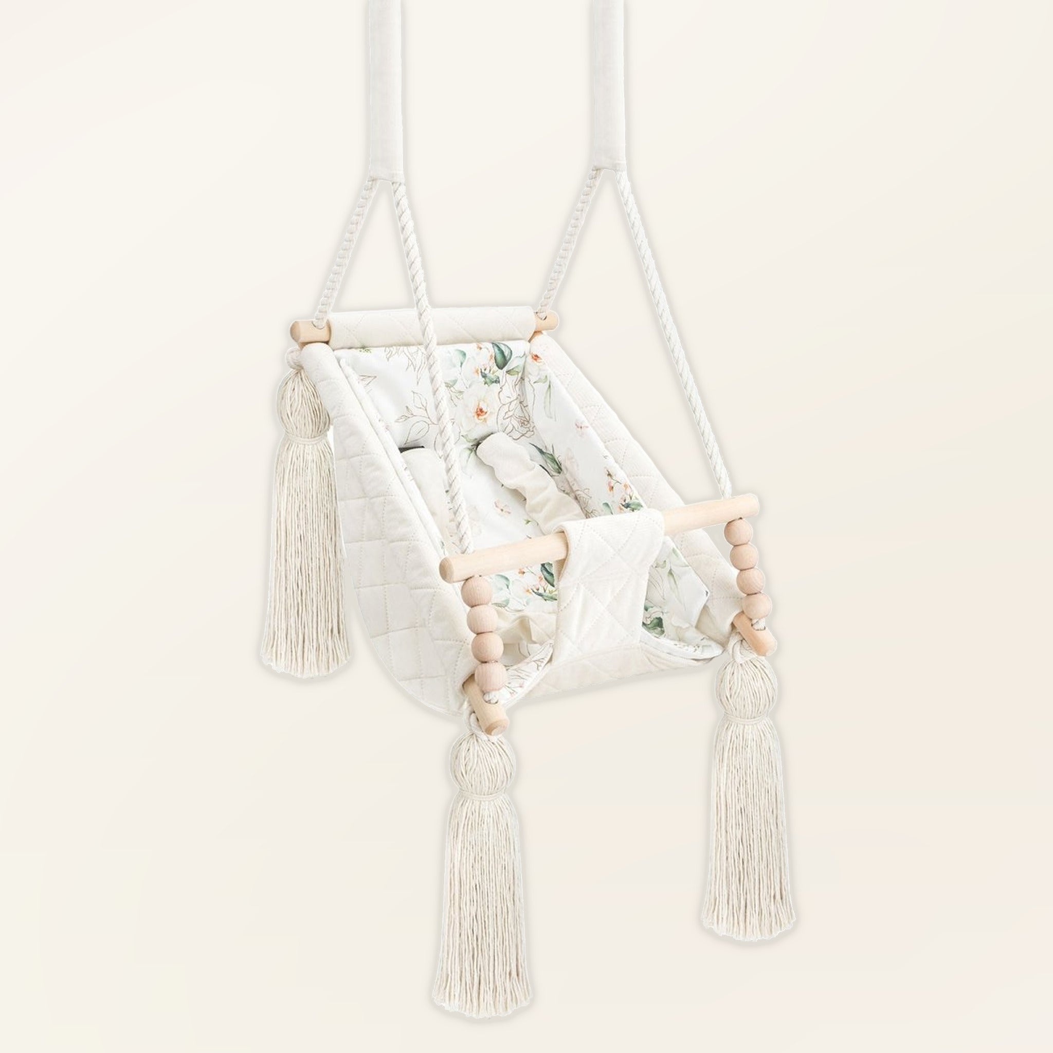 Hamac bébé suspendu en velours beige, vue de trois quarts : pompons, perles en bois et assise rembourrée