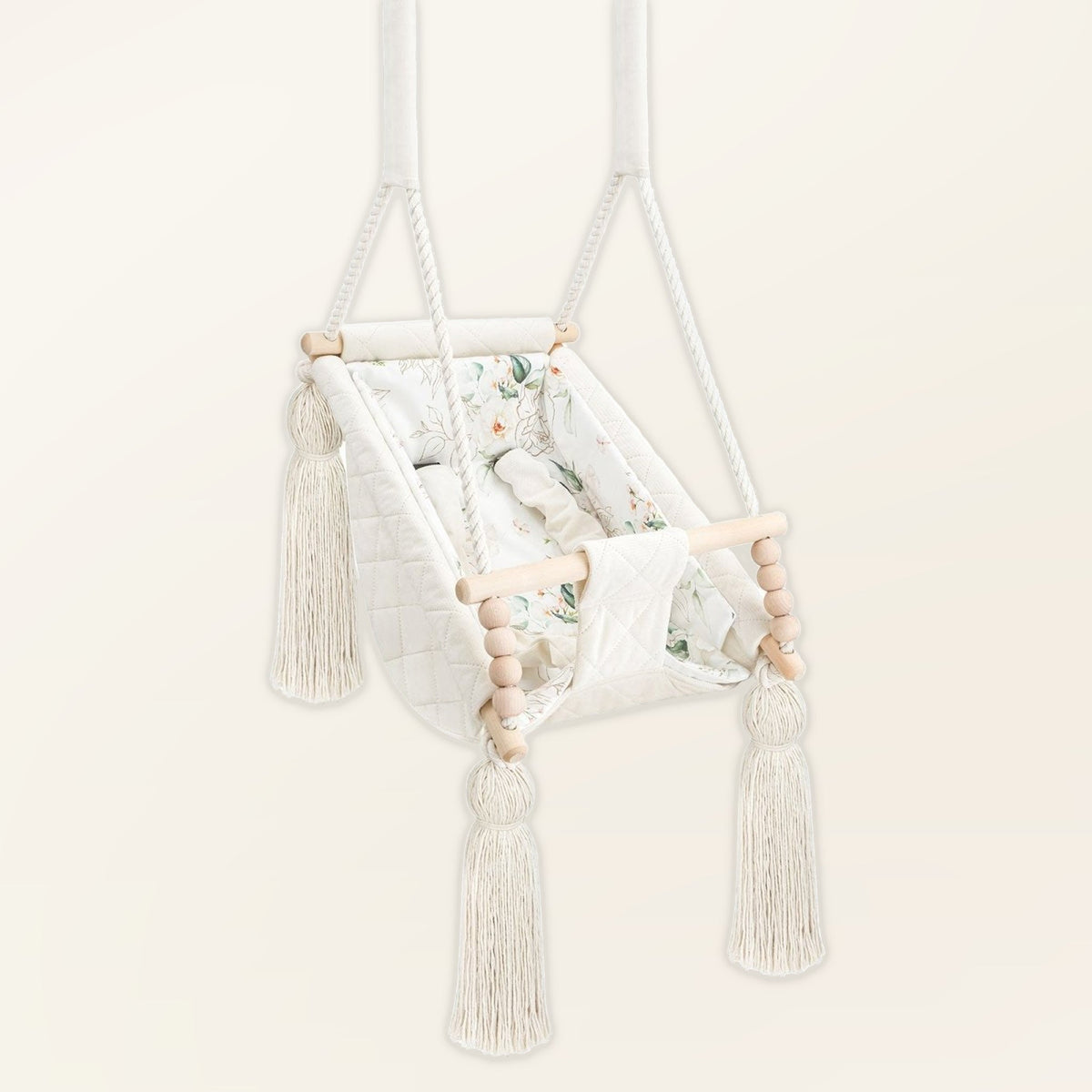 Hamac bébé suspendu en velours beige, vue de trois quarts : pompons, perles en bois et assise rembourrée