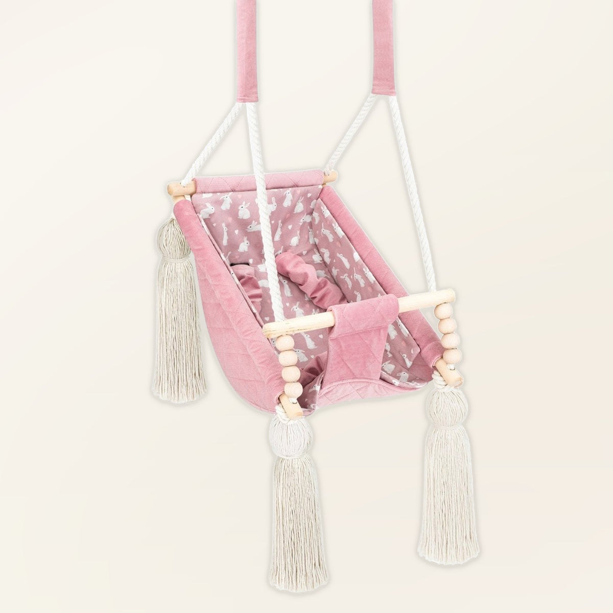 Hamac bébé suspendu en velours rose, vue de trois quarts : pompons, perles en bois et assise rembourrée