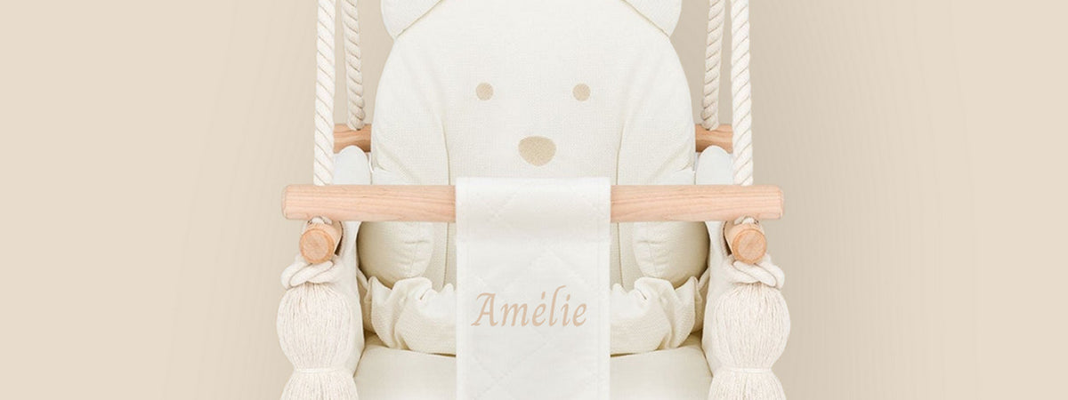 Gros plan sur une balançoire bébé en velours beige avec le prénom Amélie brodé sur le harnais